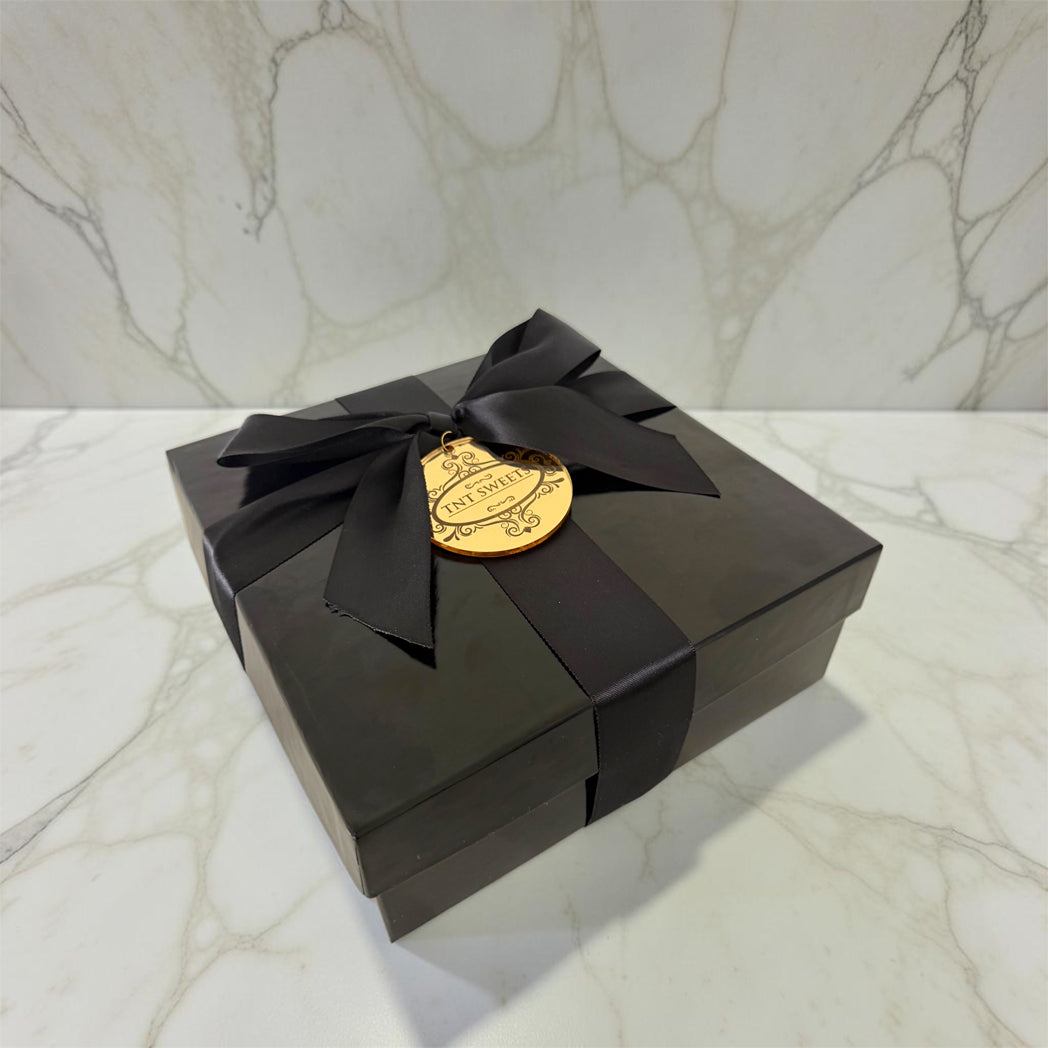 Black gift box with a gold label and black ribbon on a marble surface