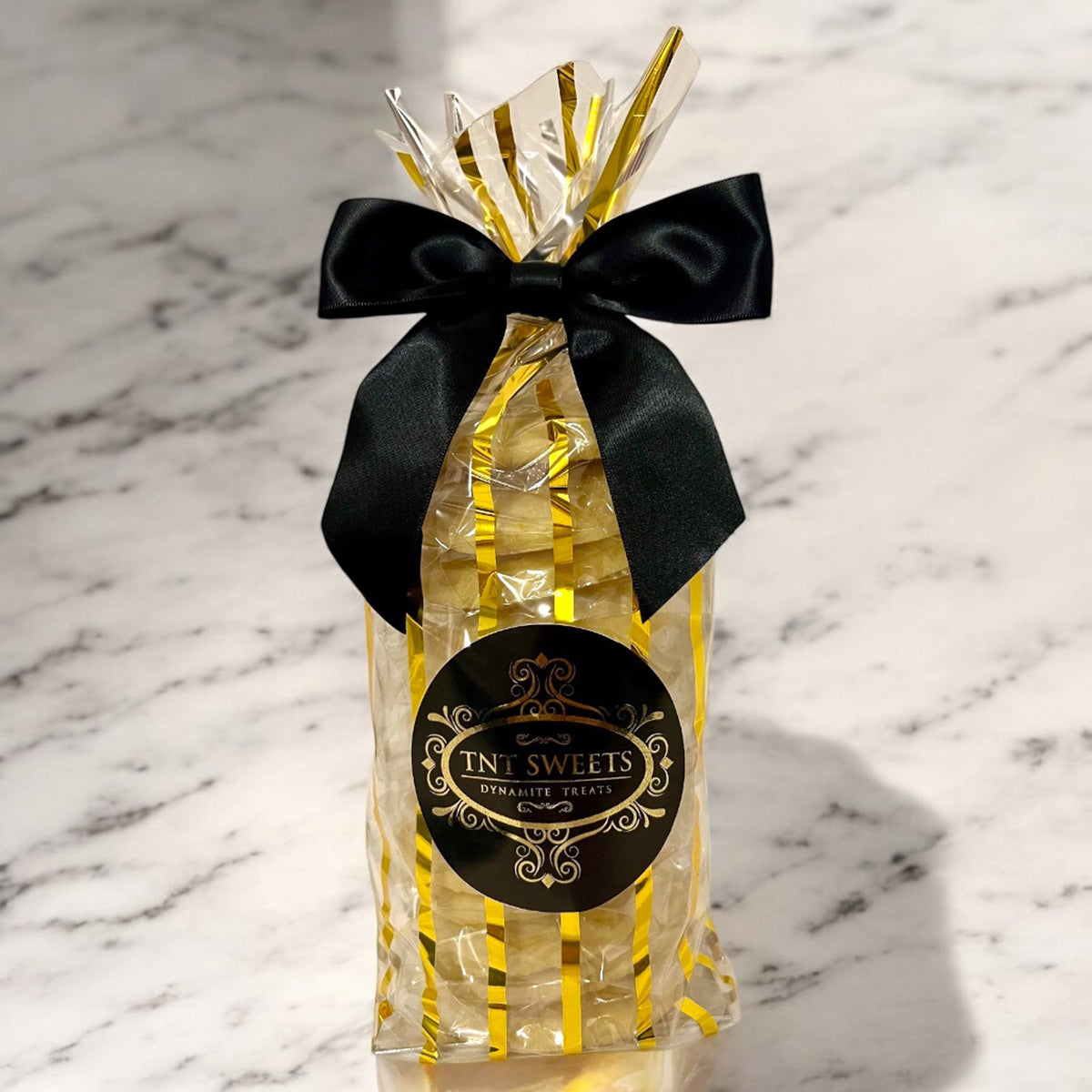 Lemon cookies in a gold striped gift bag with a black bow on a marble countertop.