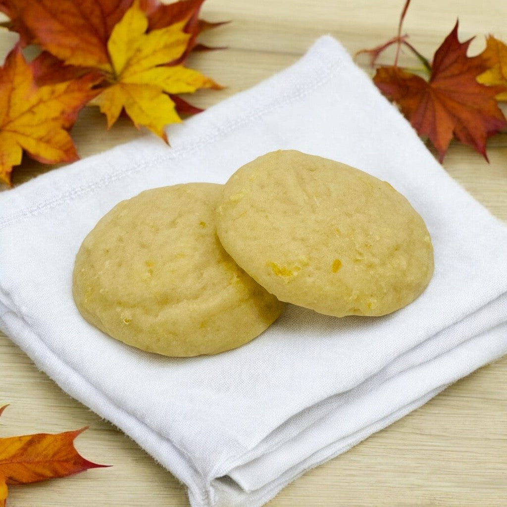 Two lemon glazed cookies on a white linen napkin on a wood countertop with scattered fall leaves.