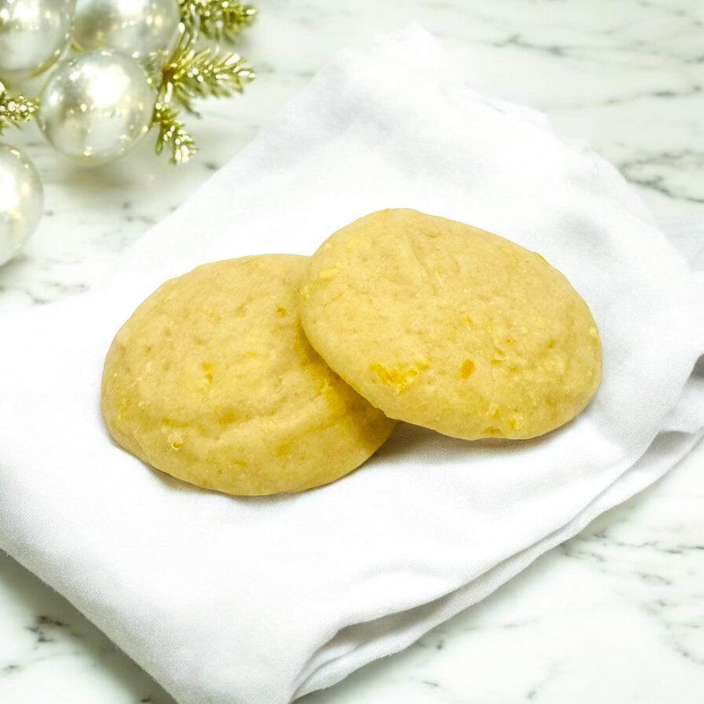 Two lemon glazed cookies on a white linen napkin on a marble countertop with white and gold decor in the background.