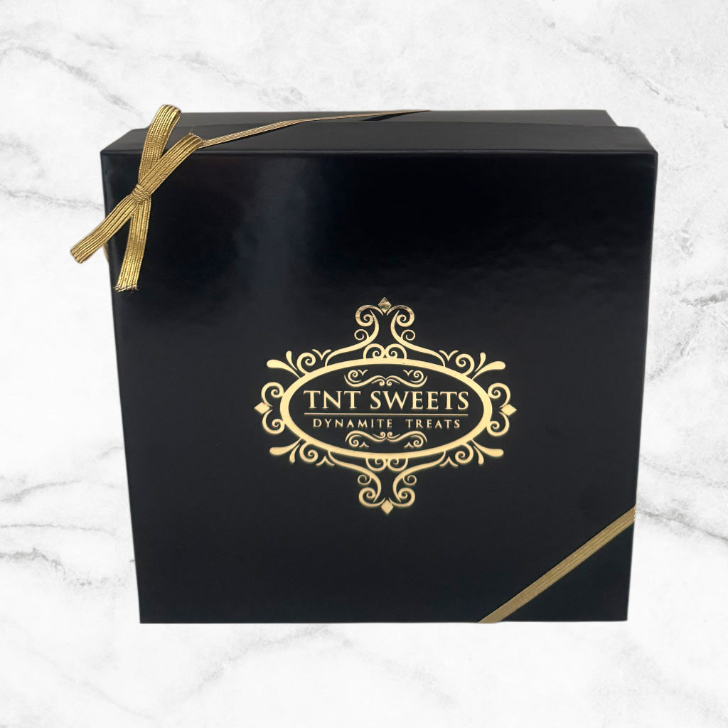 Black box with gold bow and 'TNT Sweets' logo on a white marble background