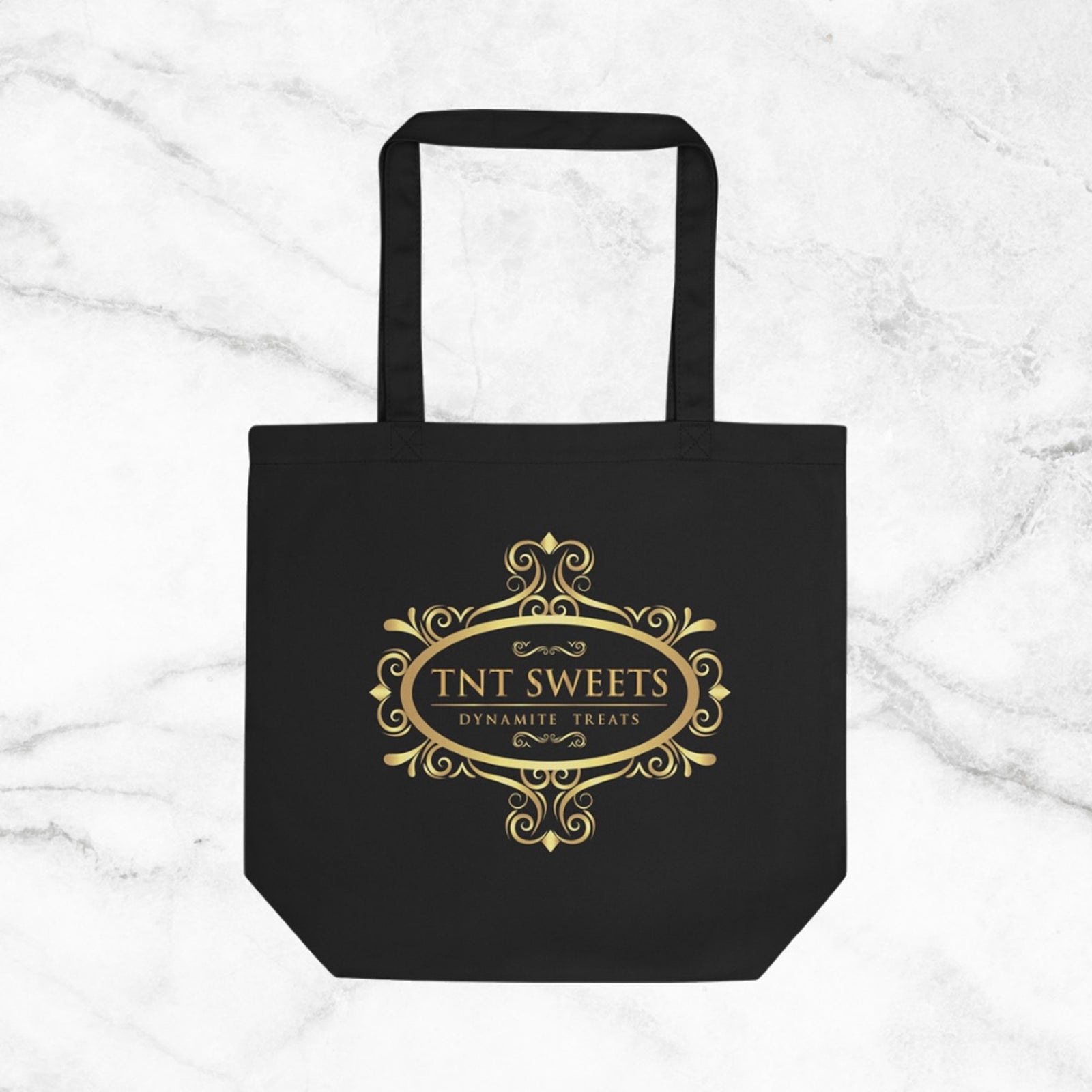 Black tote bag with gold TNT Sweets logo on a marble background.