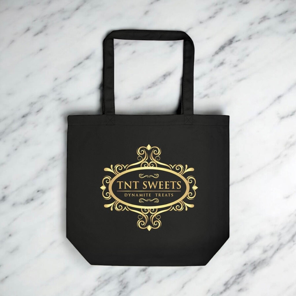 Black tote bag with gold TNT Sweets logo on a marble background.