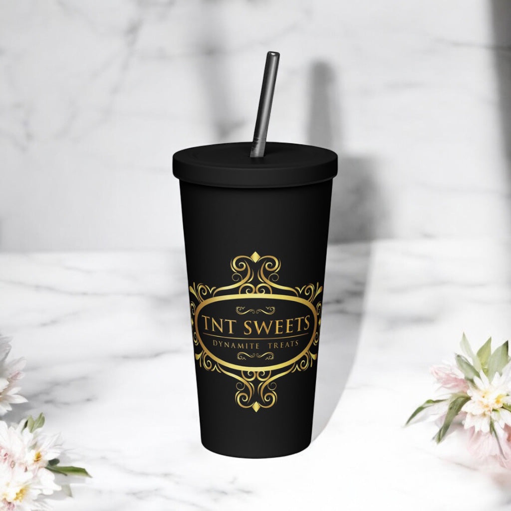 Signature black tumbler with gold logo on white marble countertop with scattered spring flowers.