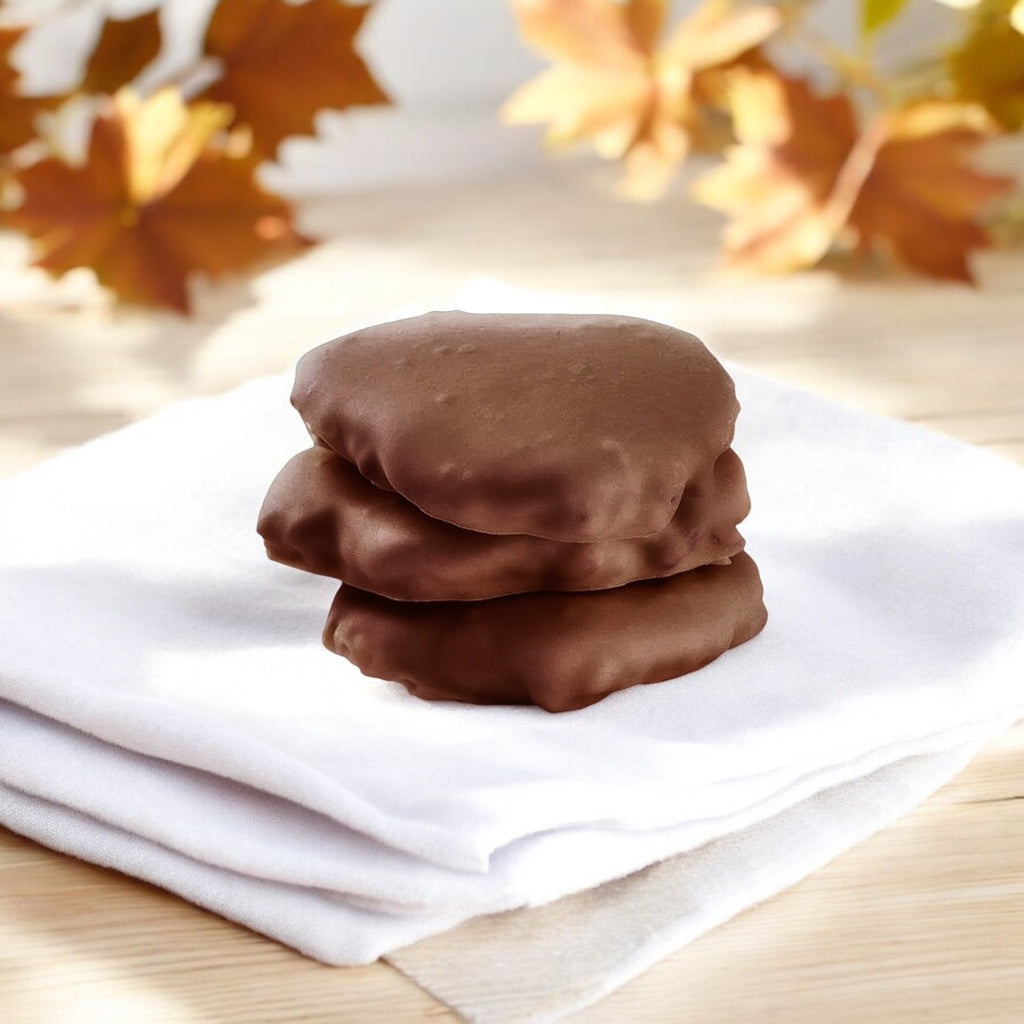 Stack of three Milk Chocolate chews on a wooden countertop with fall leaves in the background.