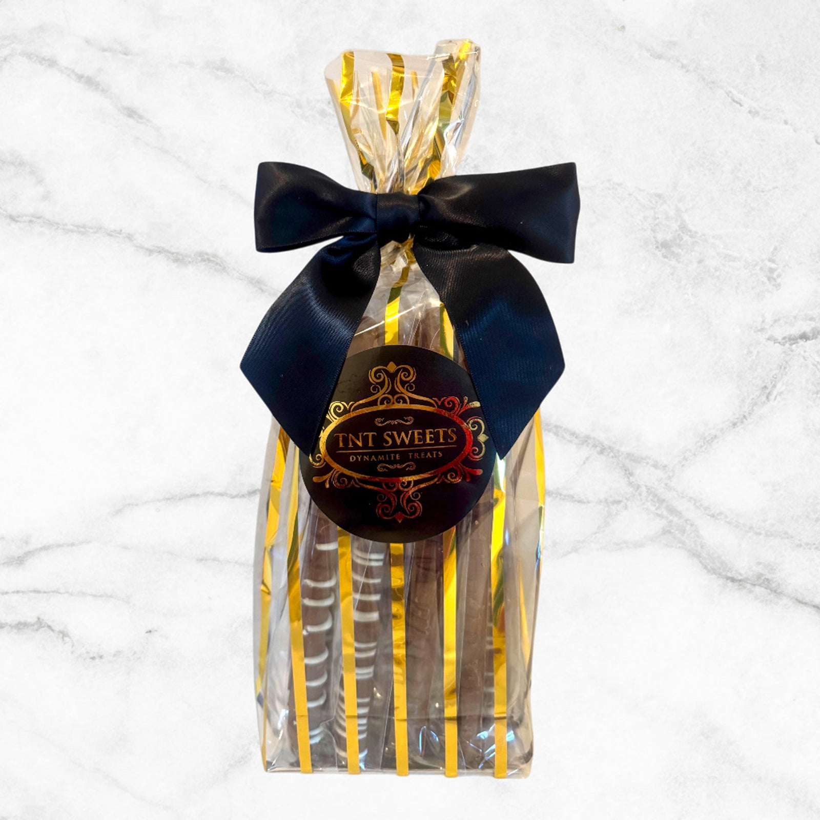 Milk chocolate pretzels in a gold striped gift bag on a white marble background.