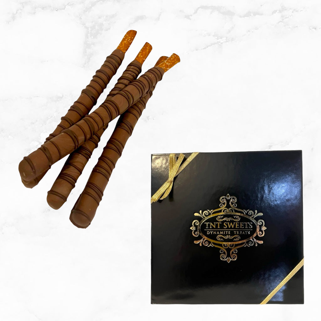 Milk chocolate dipped pretzels next to a black and gold gift box on a white marble countertop.