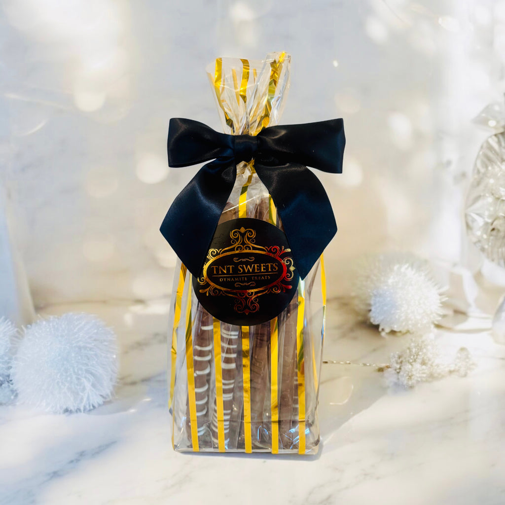 Milk chocolate pretzels in a gold striped gift bag with a black bow on a marble countertop with white decor in the background.