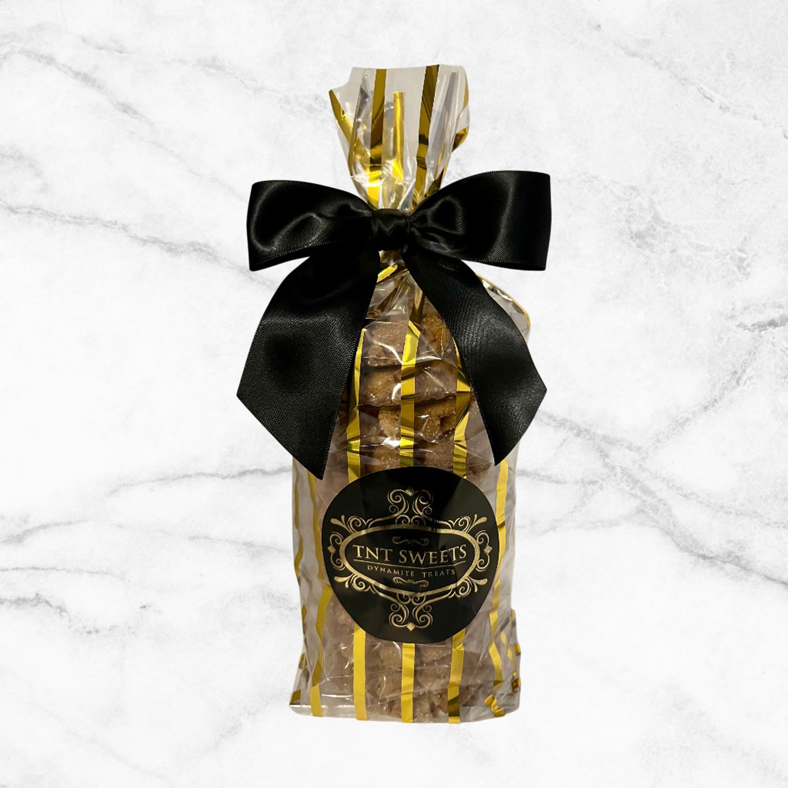 Twelve cookies in a gold striped gift bag with a black bow and logo on a white marble background. 