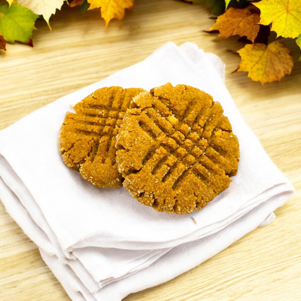 Two peanut butter cookies on a linen napkin with fall leaves in the background.