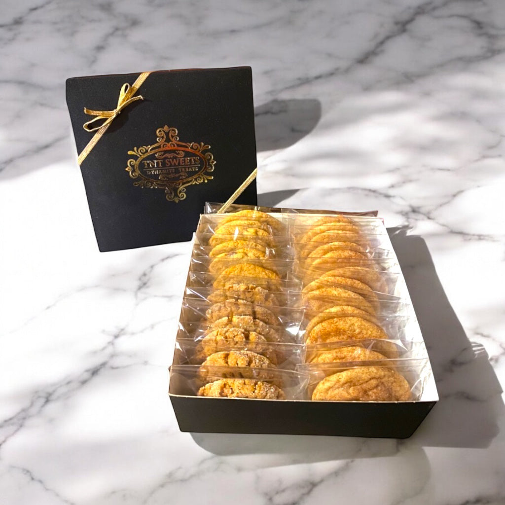 Assorted cookies in a black gift box with gold logo on a marble countertop.