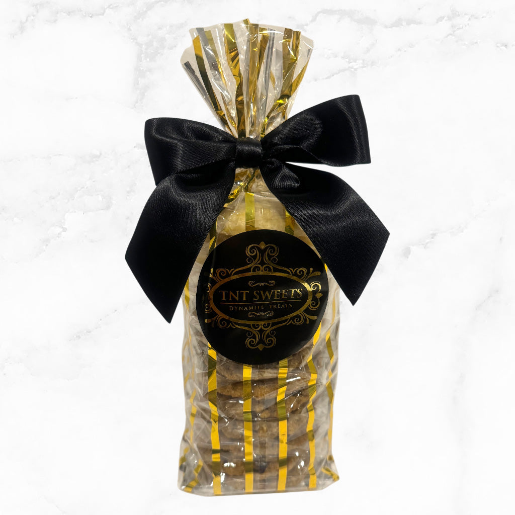 One dozen cookies assorted in a gold striped gift bag with a black bow on a marble background.