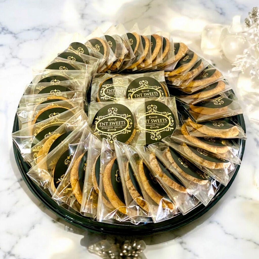 An assortment of three dozen cookies on a black cookie platter on a marble countertop with white and gold decor.