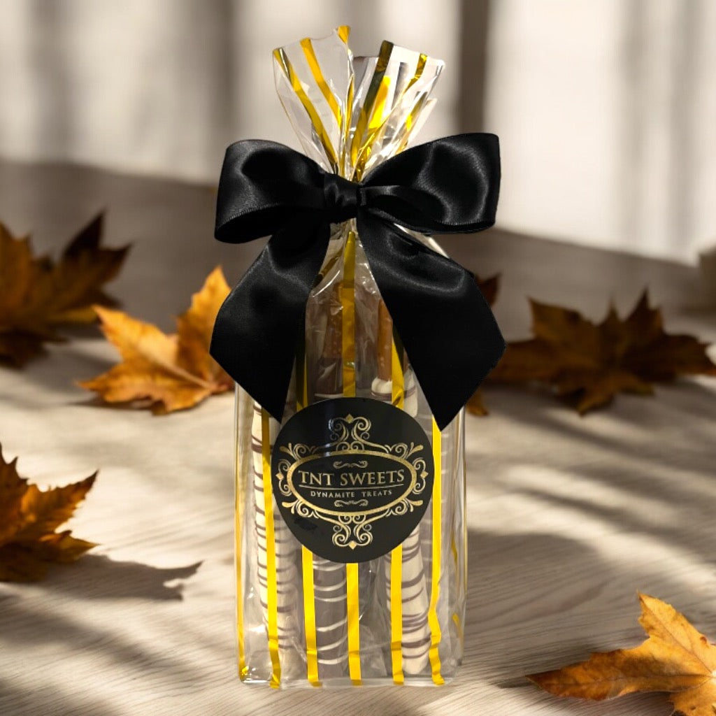 White chocolate, milk chocolate and dark chocolate pretzels in a gold striped bag on a wooden countertop with scattered fall leaves in the background.