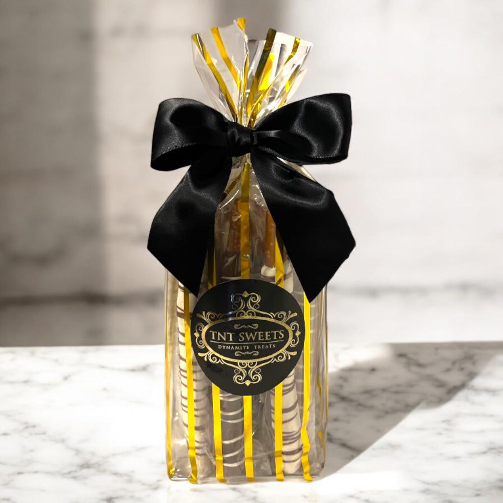 Pretzel medley in a gold striped gift bag with a black bow and label on a marble countertop.