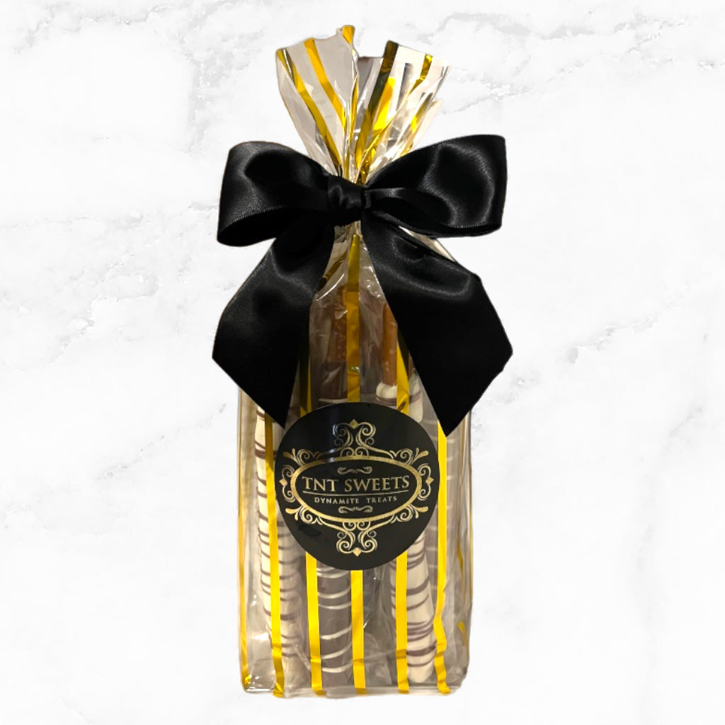 Pretzel medley in a gold striped gift bag with a black bow and label on a marble countertop.