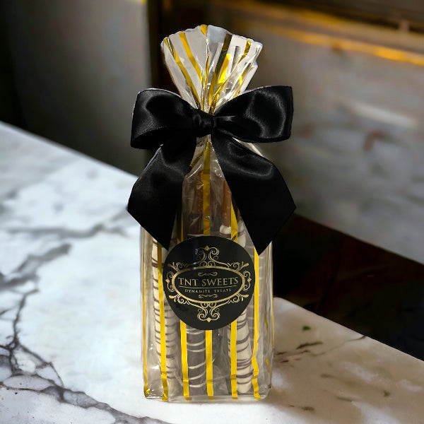 White chocolate, milk chocolate and dark chocolate pretzels in a gold striped bag on a white marble countertop.