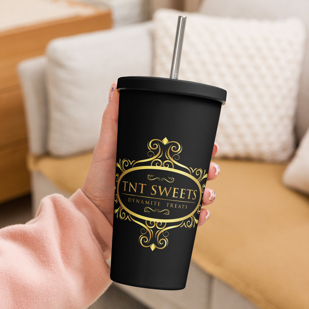 Person holding signature black tumbler with a gold logo with a blurred living room background. 