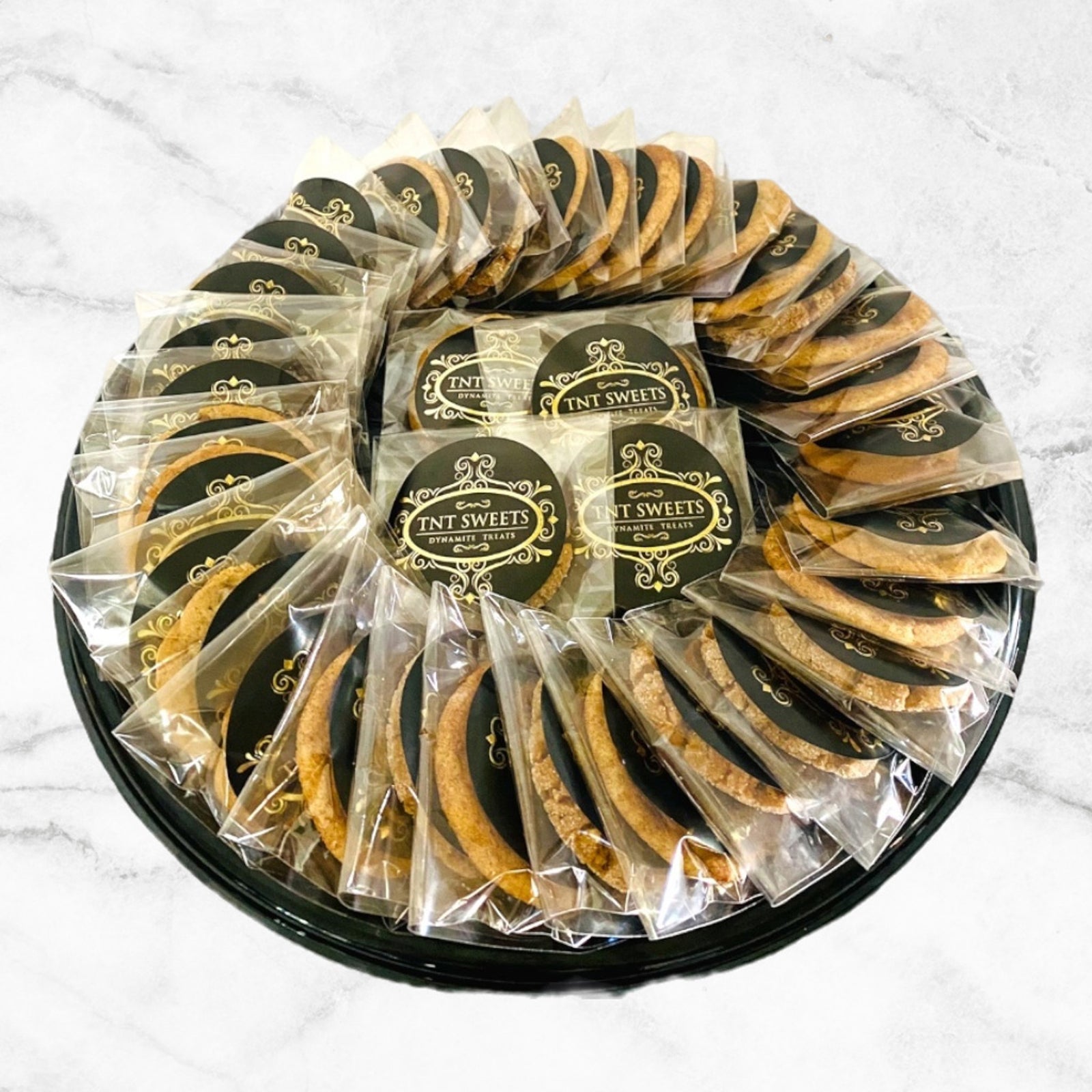 Three dozen cookies individually wrapped on a black platter on a white marble countertop.