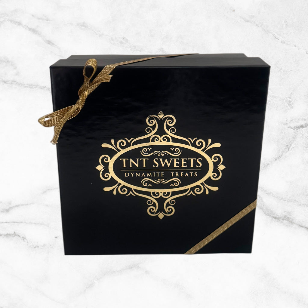 Black and gold gift box with a gold logo, finishes with a gold ribbon on a white marble background.