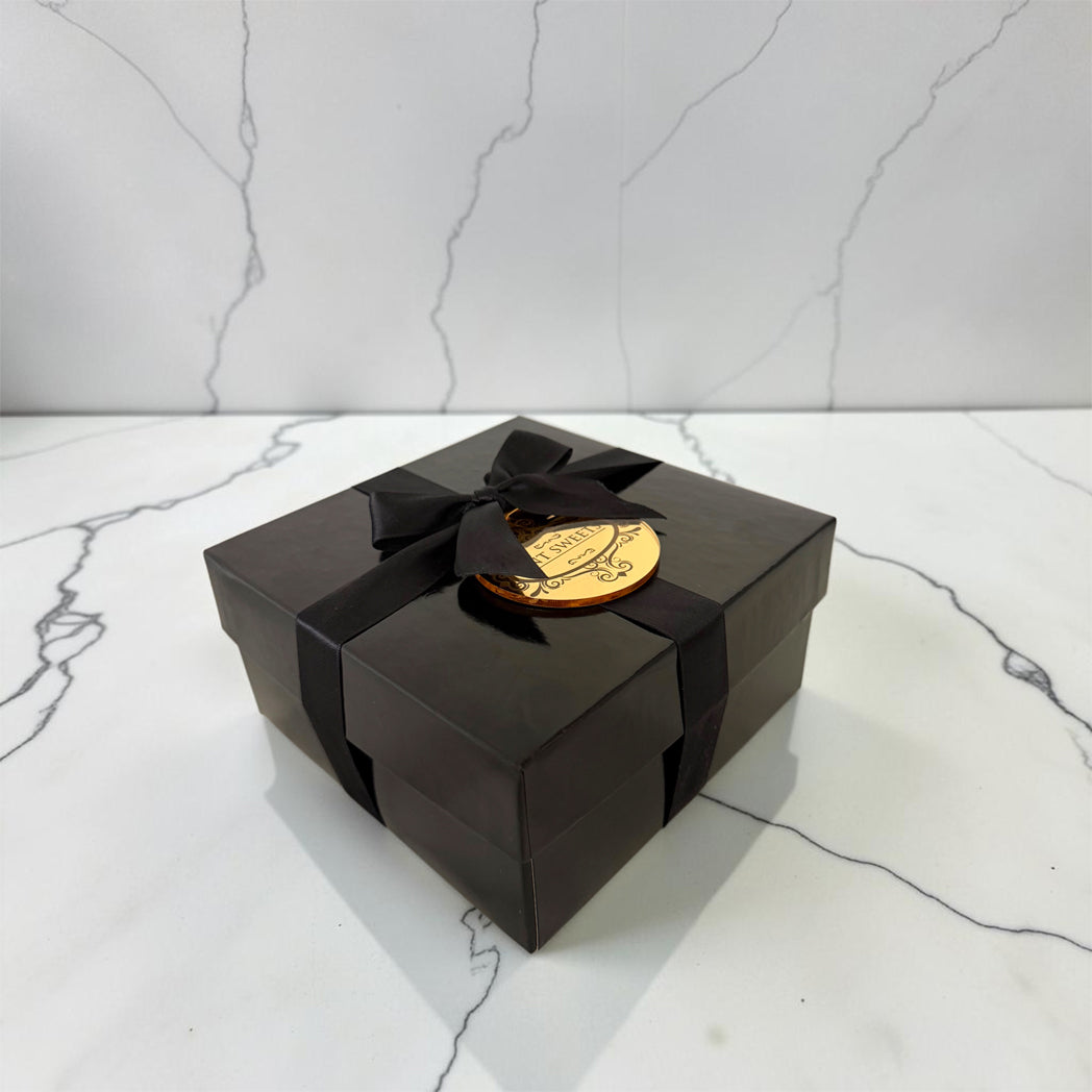 Small black gift box tied with black ribbon, gold medallion and white marble background.