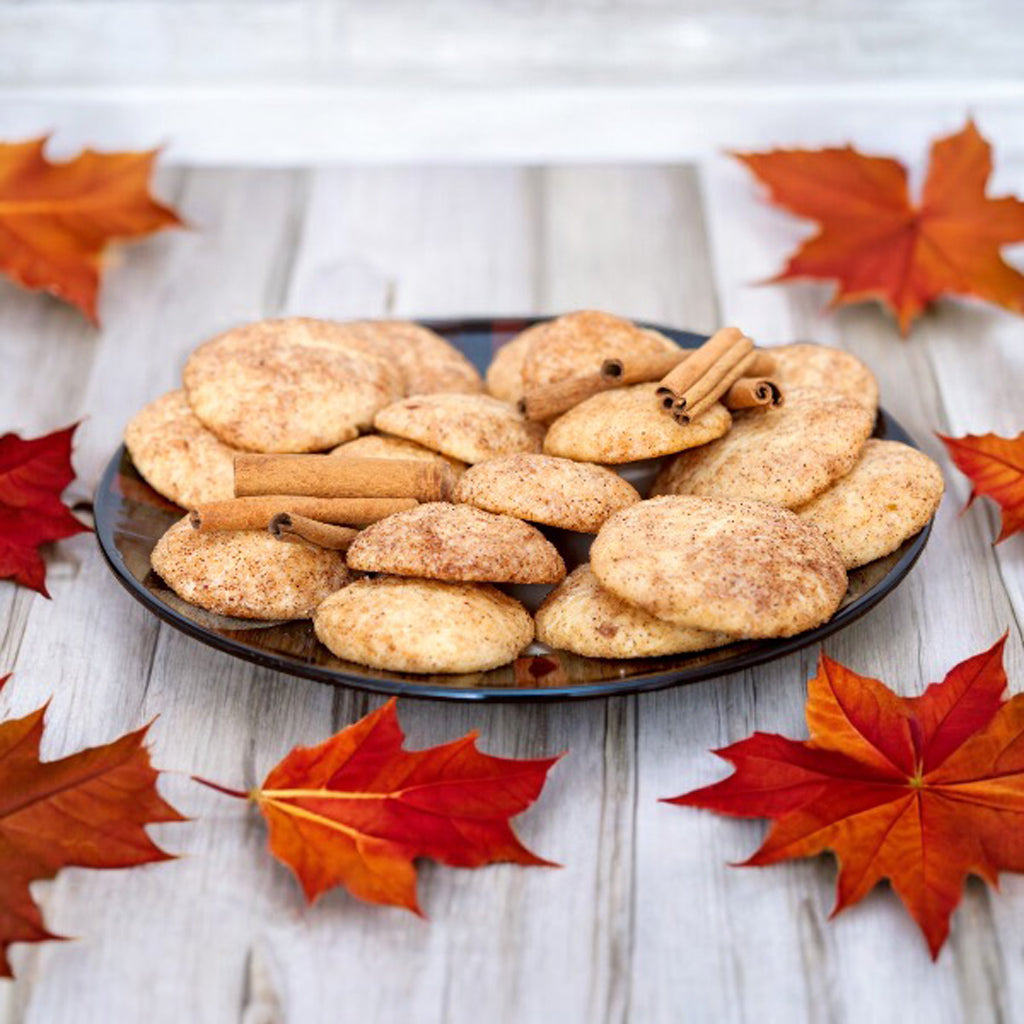 Plate of snickerdoodle cookies with cinnamon sticks with scattered fall leaves on a wooden countertop.