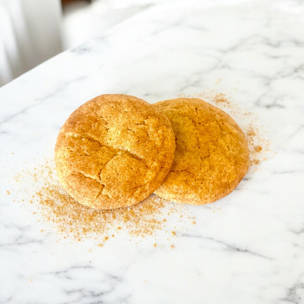 Spiced sugar cookies on a white marble countertop dusted with cinnamon. 