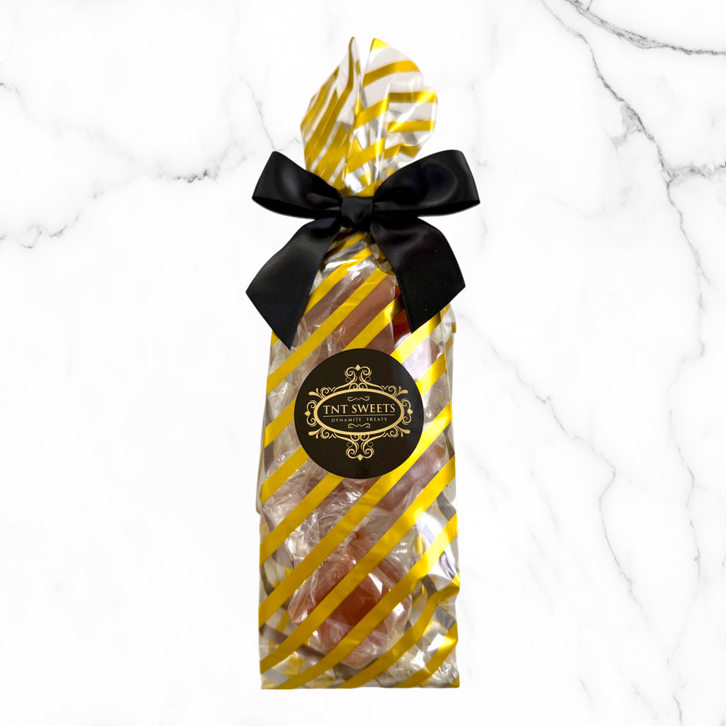 Packaged candy with yellow and white striped wrapping and black bow on a marble background