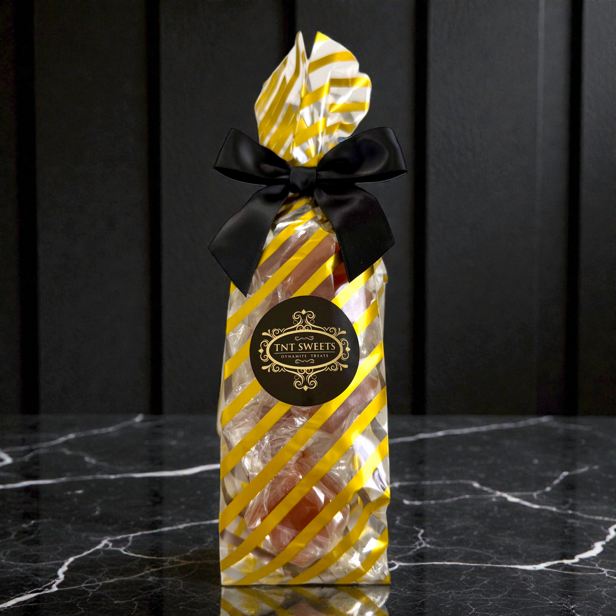 Caramels in a gold and white striped design and black bow on a dark marble surface.