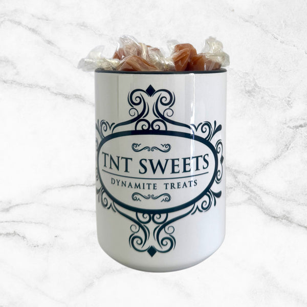 15oz TNT Signature White Mug filled with caramels on a white marble background.