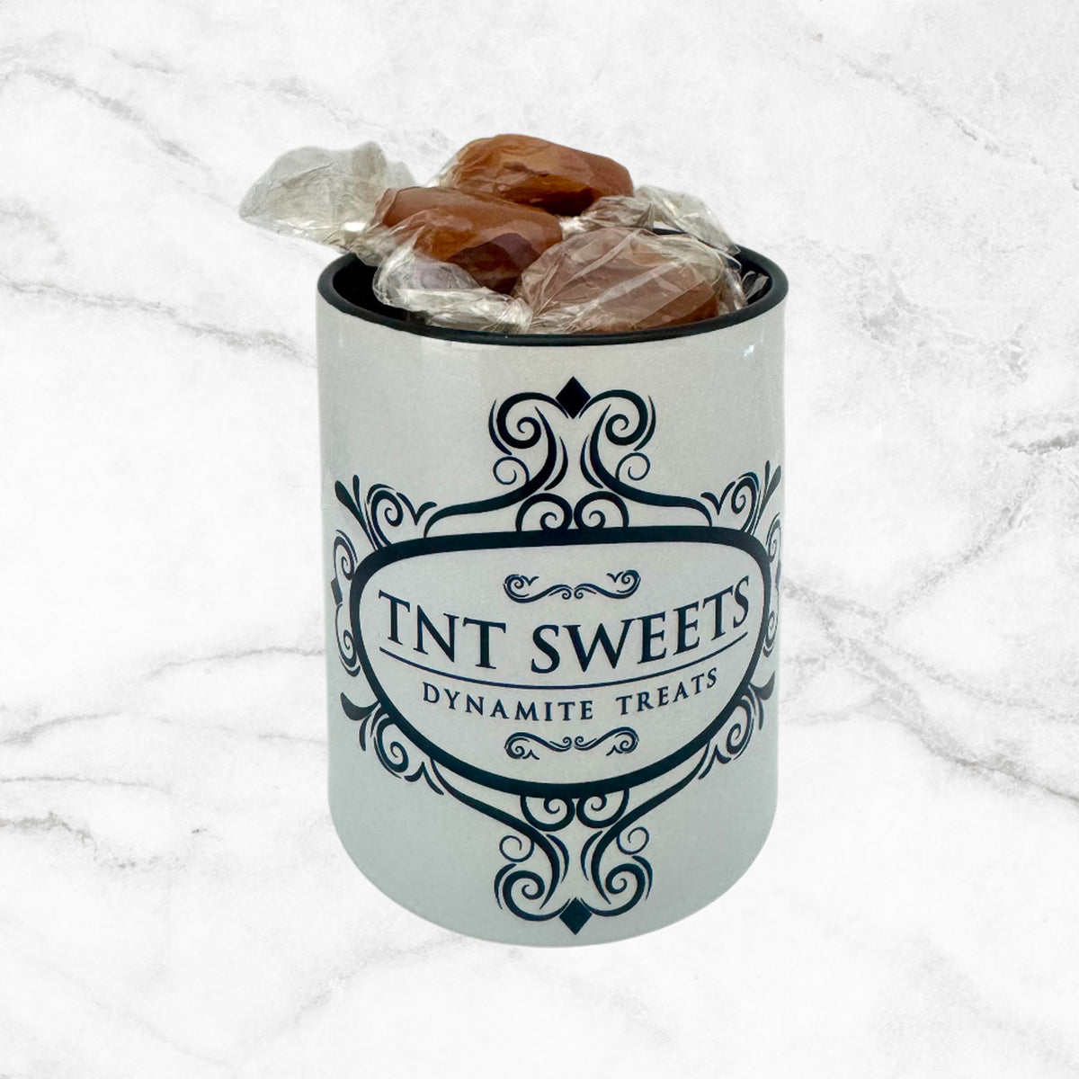 11oz TNT Sweets Alabaster Edition Caramel-filled Mug with Caramels unwrapped with a black handle on the side on a white marble background.