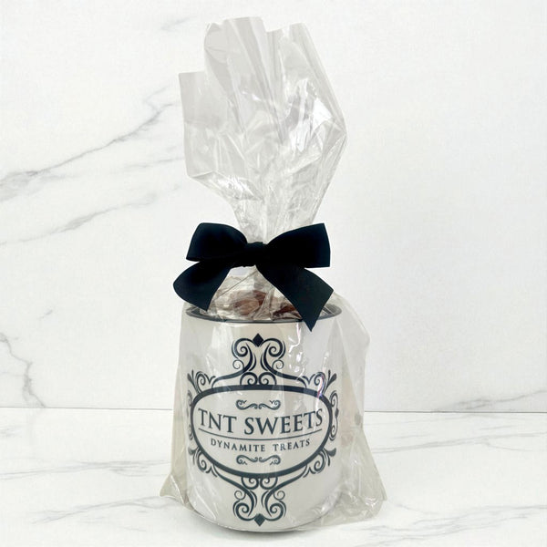 11 oz TNT Signature White Mug filled with caramels wrapped in cellophane with a black bow and black logo on a white marble background.