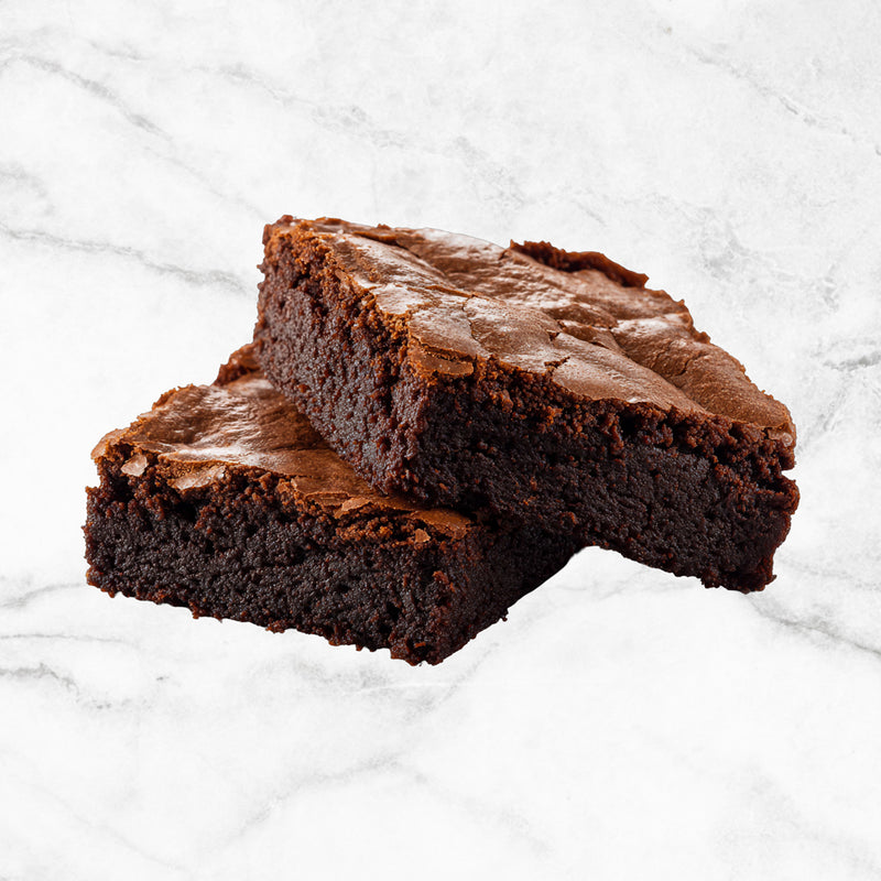 The Alchemist, two milk chocolate brownies from TNT Sweets made with Callebaut Belgian milk chocolate and gluten-free on a white marble surface.