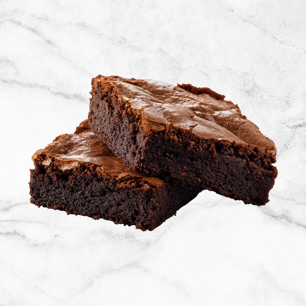 The Alchemist, two milk chocolate brownies from TNT Sweets made with Callebaut Belgian milk chocolate and gluten-free on a white marble surface.