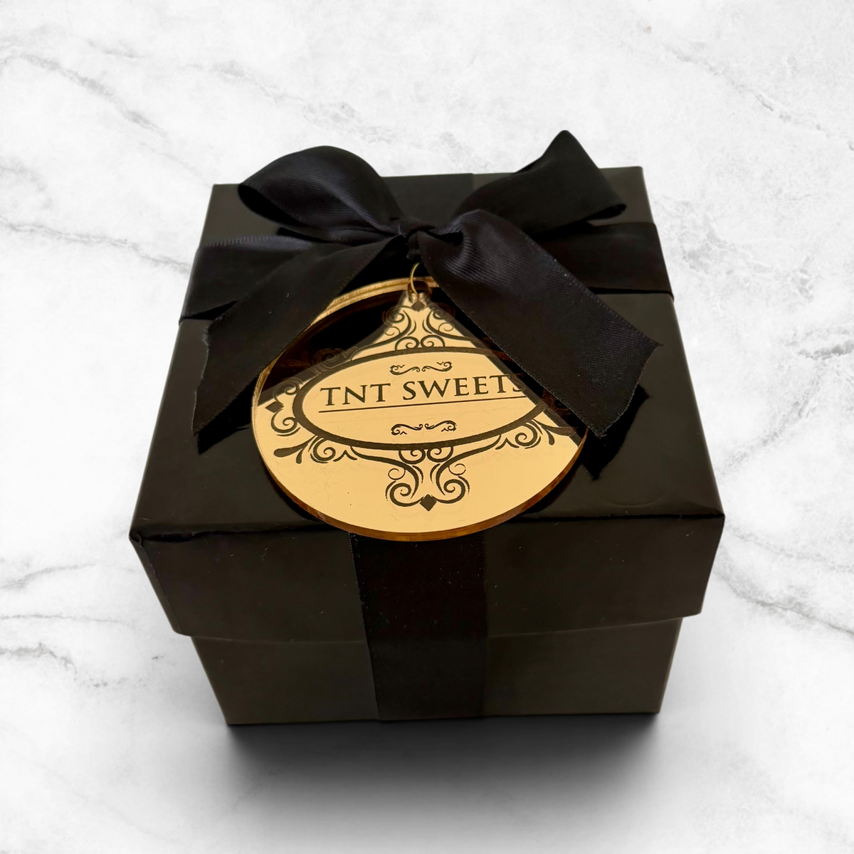 Black gift box with a gold label and black ribbon on a white marble surface