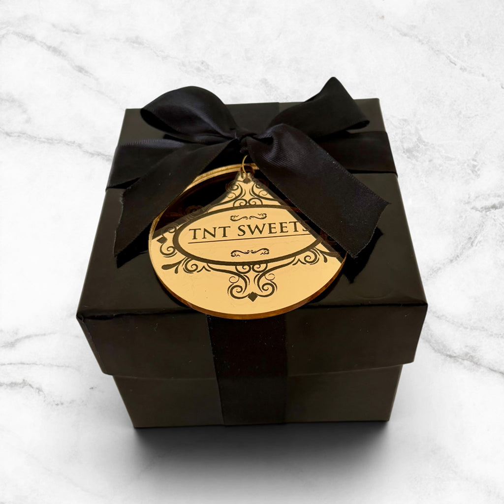 Black gift box with a gold label and black ribbon on a white marble surface