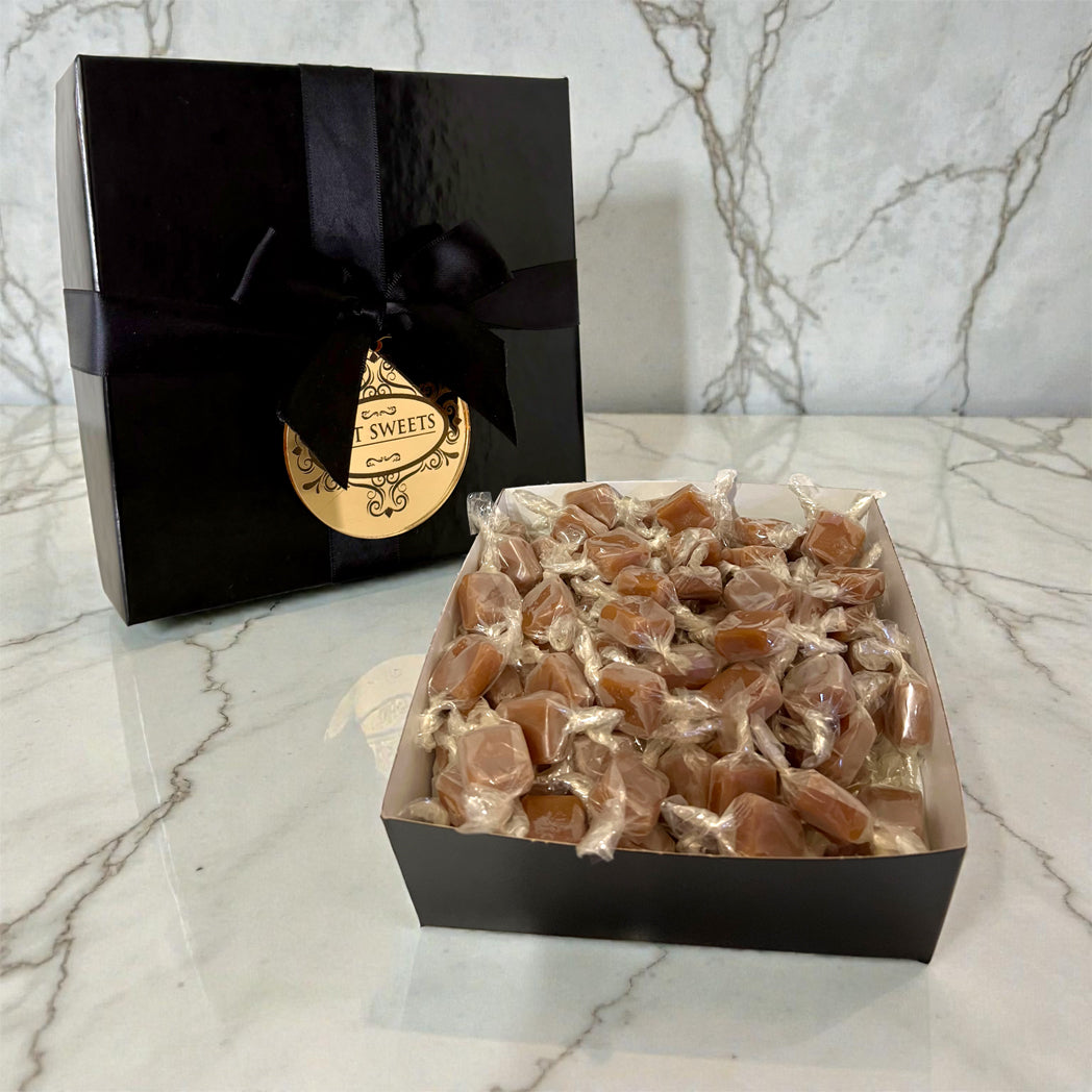 Box of caramels with a black gift box on a marble surface