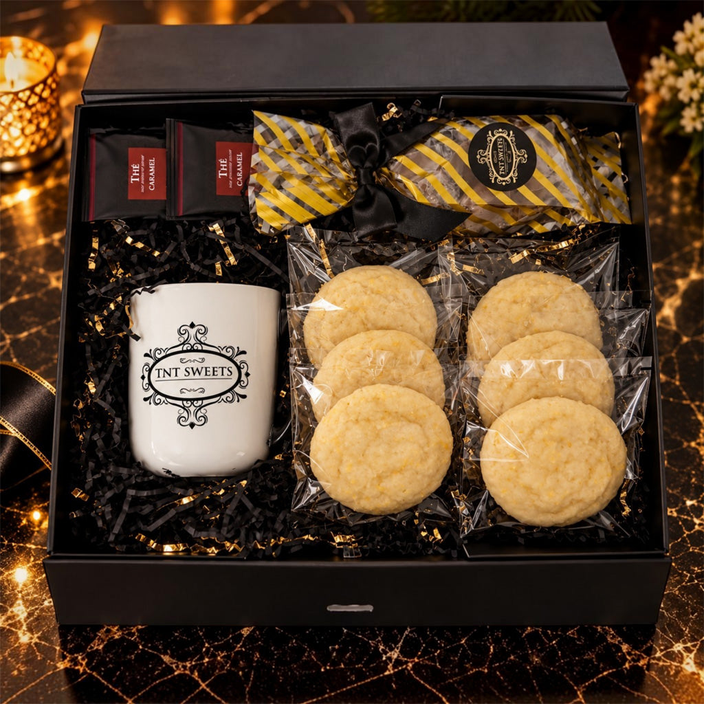 TNT Sweets Black Tie Curation open gift box with six cookies, handcrafted caramels, two Damman Freres tea packets, and a white logo mug nestled in black-and-gold shred.
