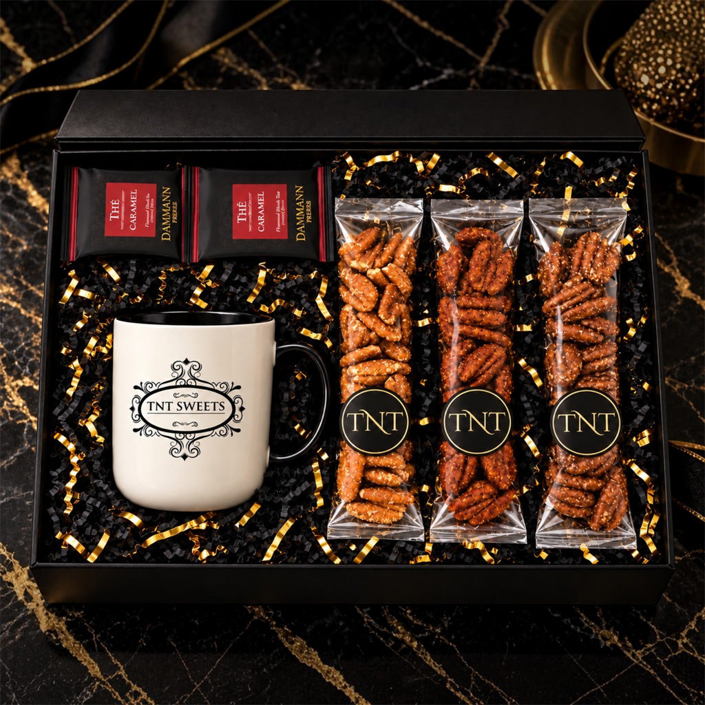 TNT Sweets Black Tie gift box featuring a signature mug, two Damman Freres tea sachets, and three varieties from The Pecan Reserve in black and gold packaging on a black and gold marble background.