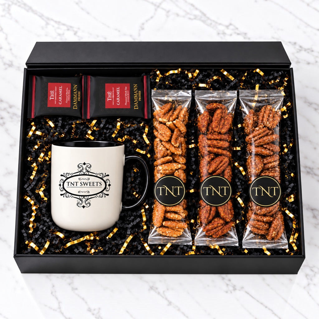 TNT Sweets Black Tie gift box featuring a signature mug, two Damman Freres tea sachets, and three varieties from The Pecan Reserve in black and gold packaging on a white marble background.