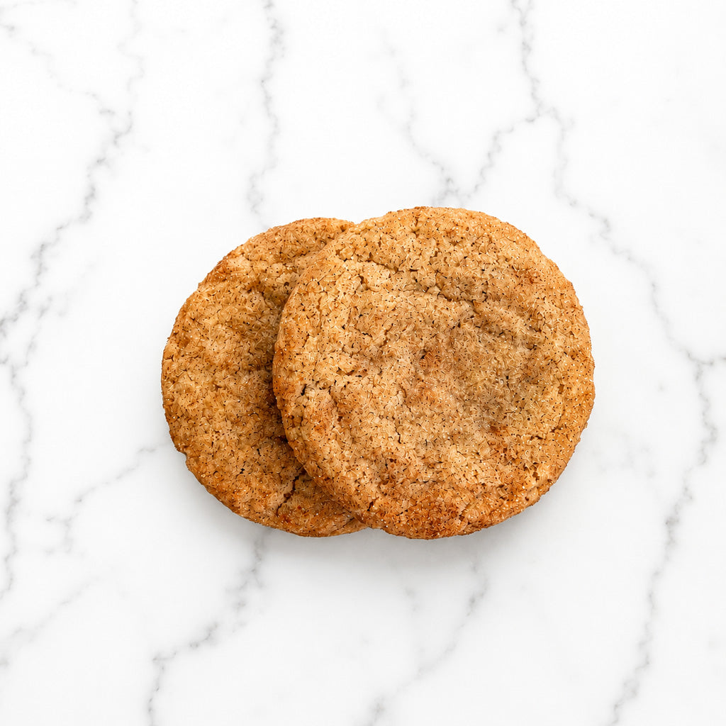 Two Copper Spice snickerdoodle cookies made with Ceylon cinnamon and Madagascar vanilla on a marble background.