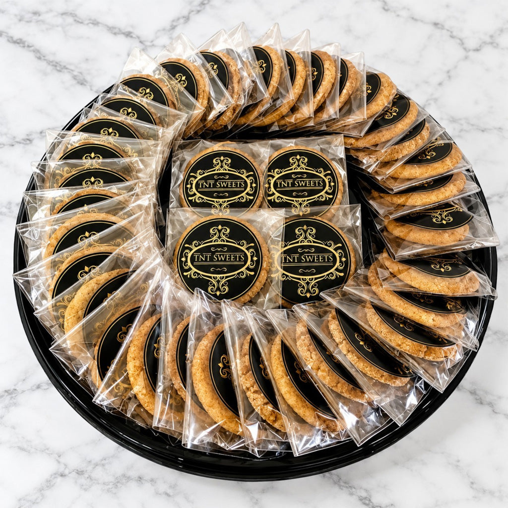 The Grand II 60 count cookie assortment on a black platter individually wrapped with the TNT Sweets seal on a white marble background. 