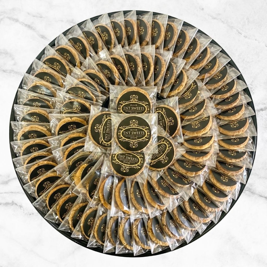 The Grand II (60-piece) cookie platter by TNT Sweets featuring individually wrapped artisan cookies arranged in an elegant circular presentation, customized with your choice of signature flavors on a white marble background.