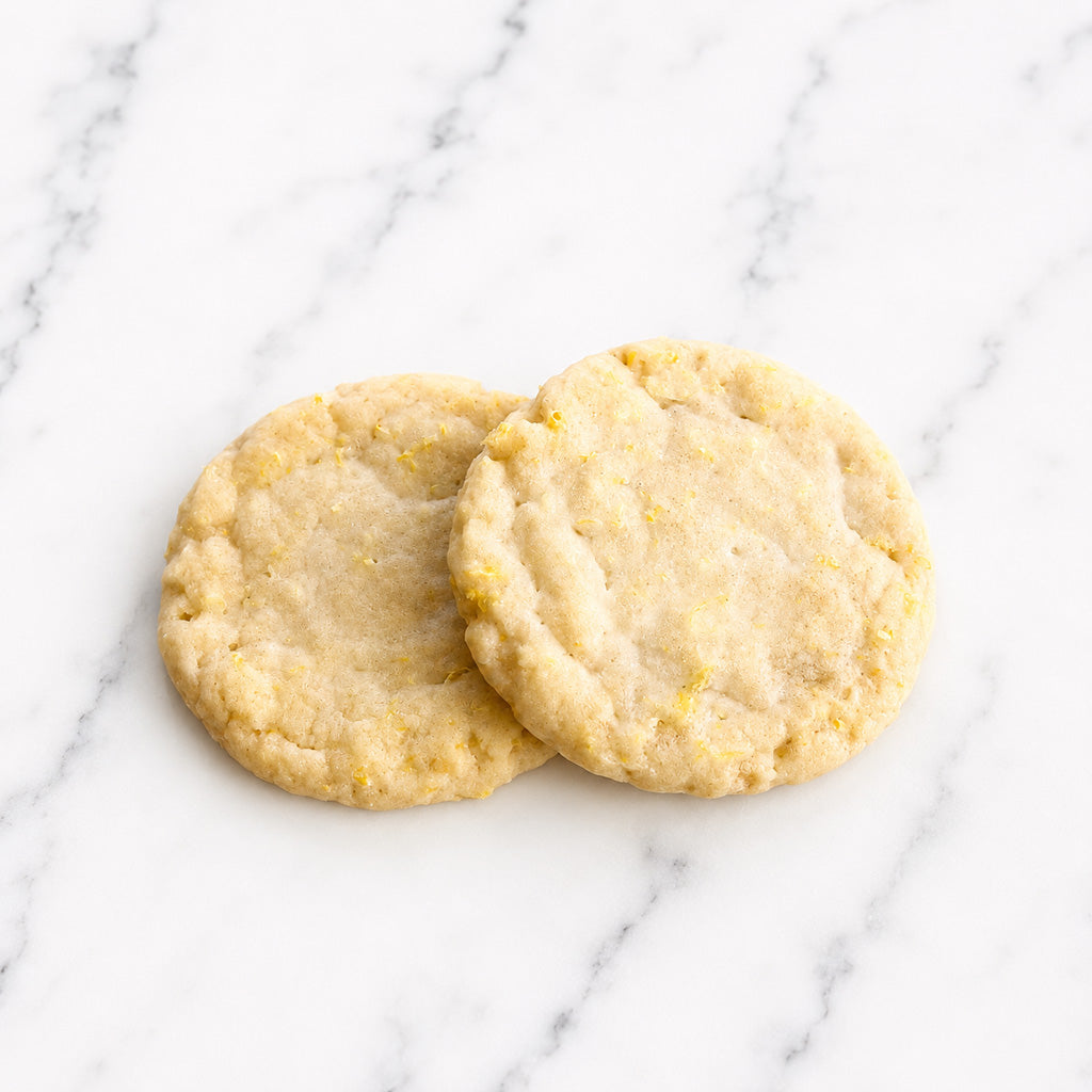 Two Lumière lemon cookies on a white marble background.