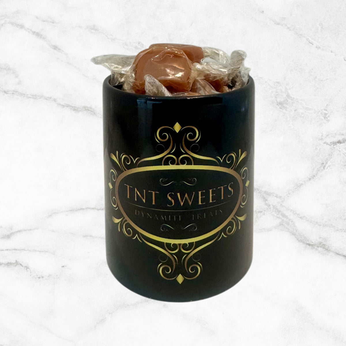11oz TNT Signature black mug filled with caramels on a white marble background.