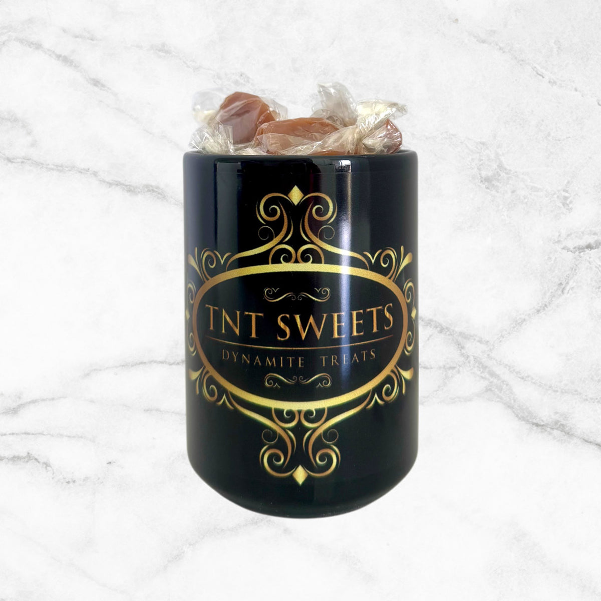15oz TNT Signature black mug filled with caramels on a white marble background with an front view.