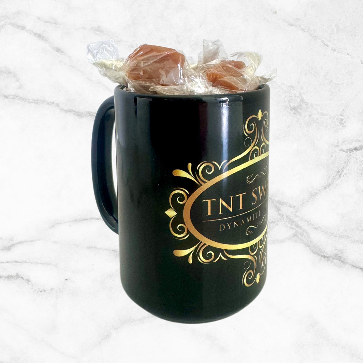 15oz TNT Signature black mug filled with caramels on a white marble background with an angled view.