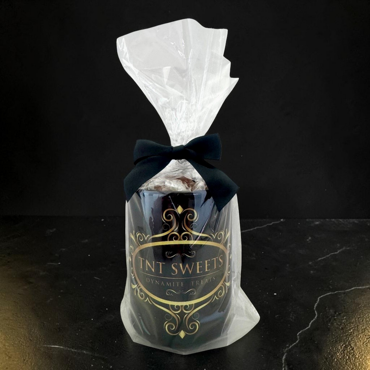 TNT Sweets 15-ounce Obsidian Edition mug gift wrapped in clear cellophane with a black satin bow.