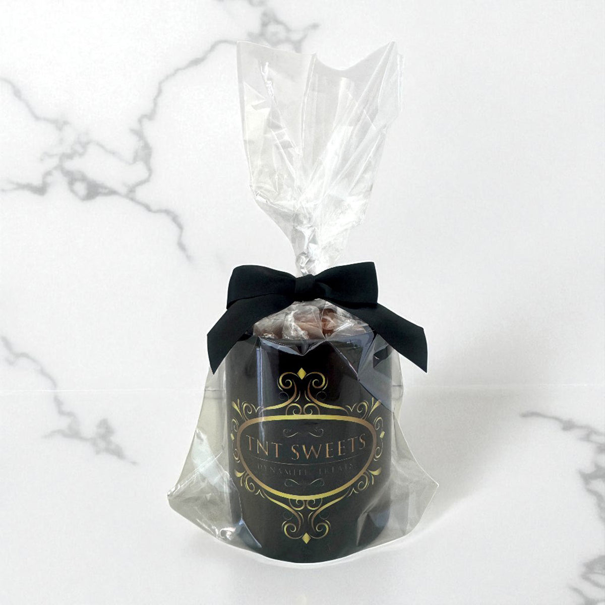 11oz black gift mug filled with caramels wrapped in cellophane with a black bow and a gold TNT logo on a white marble background.