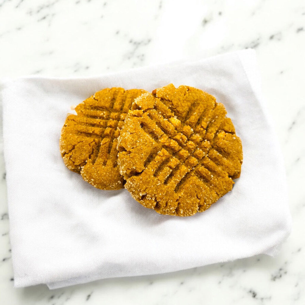 Two Peanut Butter Reserve cookies from TNT Sweets made with Madasgar vanilla on a white linen napkin on a white marble surface.